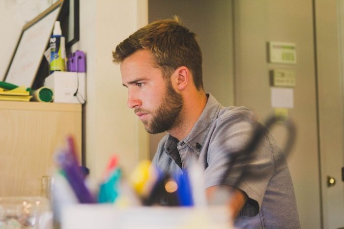 Jeune homme barbu de profil aussis à un bureau où il travaille