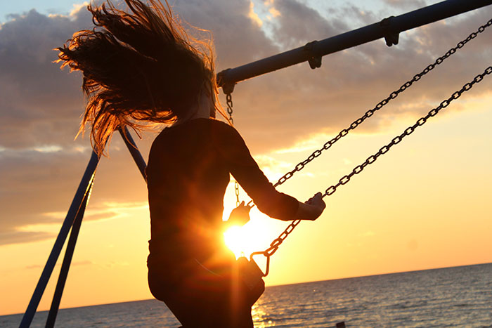 Personne sur une balançoire au coucher de soleil face à la mer