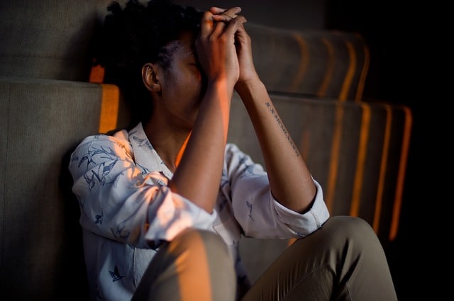 femme en chemise par terre canapé se tient la tête dans les mains, contrariée gestion du stress au travail